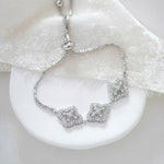 Silver Addia bridal bracelet featuring shimmering cubic zirconia quatrefoil motifs and an adjustable slider chain, styled on a white ceramic dish with soft ivory fabric.