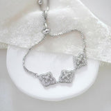 Silver Addia bridal bracelet featuring shimmering cubic zirconia quatrefoil motifs and an adjustable slider chain, styled on a white ceramic dish with soft ivory fabric.