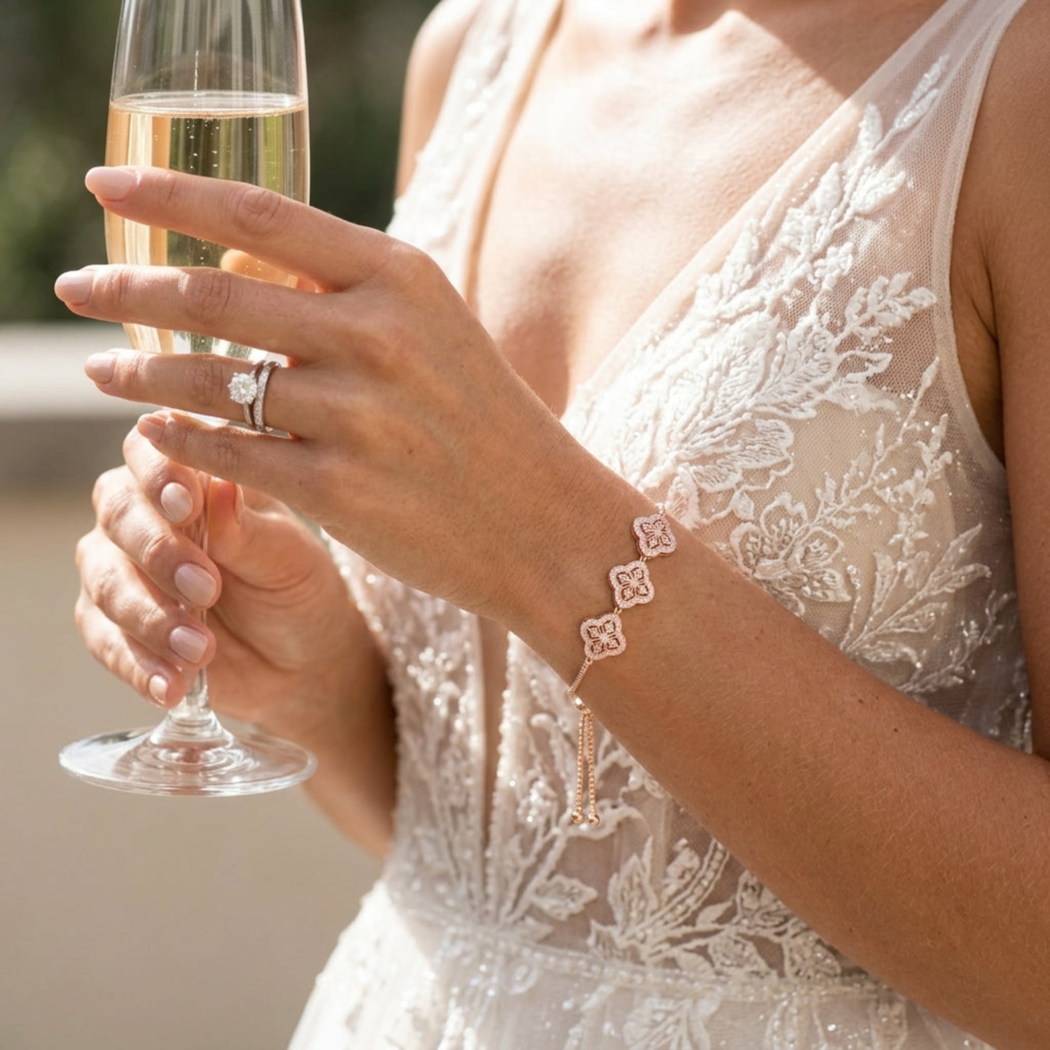 Bride wearing the Addia rose gold cubic zirconia bracelet with adjustable slider closure while holding a champagne flute, showcasing elegant bridal wrist jewelry.
