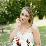 A bride wearing a strapless white lace wedding dress and holding a bouquet of white and burgundy flowers, posing outdoors in a grassy garden with a blurred green background.