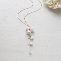 Rose gold bridal backdrop necklace featuring handcrafted white porcelain flowers, genuine freshwater pearls, and a delicate cascading drop, styled on a neutral background.