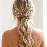 Back view of a blonde bride wearing the Cleo white opal crystal wedding hair vine above a softly waved low ponytail, styled with a romantic bridal hairstyle.