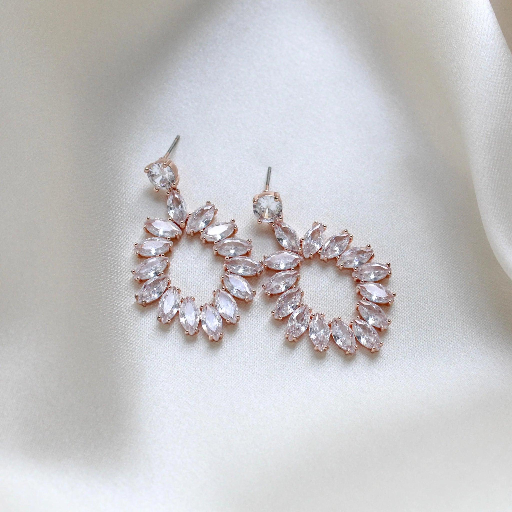 Treasures by Agnes Odette bridal earrings with marquise cut cubic zirconia in a rose gold finish on ivory satin fabric.
