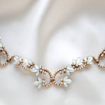 Close-up of Cleo antique gold bridal hair vine featuring Swarovski white opal crystal flowers, intricate sparkling scrollwork and hair comb attachments, displayed on soft ivory satin.