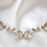 Close-up of Cleo antique gold bridal hair vine featuring Swarovski white opal crystal flowers, intricate sparkling scrollwork and hair comb attachments, displayed on soft ivory satin.