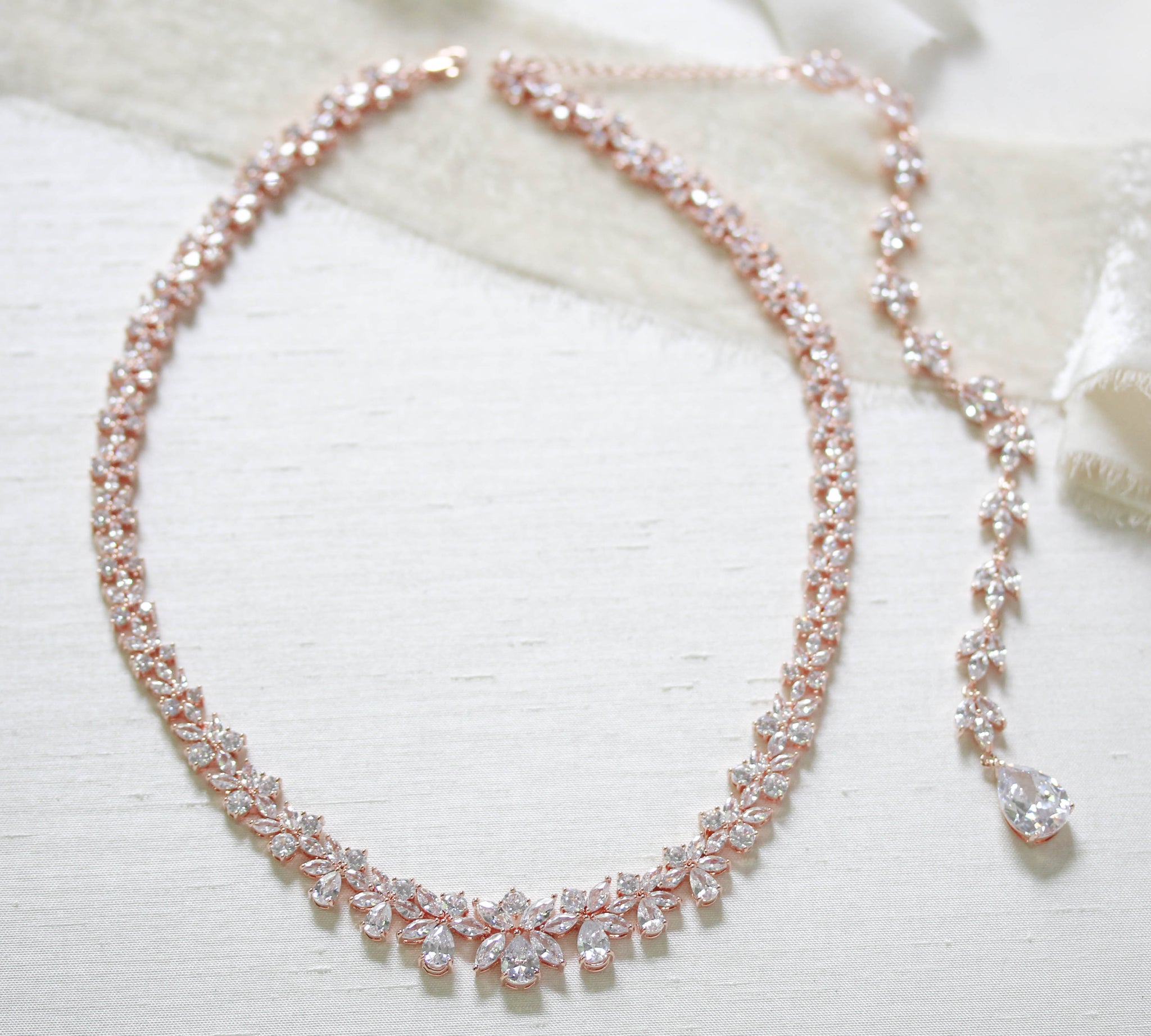 Treasures by Agnes Aubree bridal necklace with detachable cubic zirconia backdrop chain in rose gold finish displayed on ivory fabric