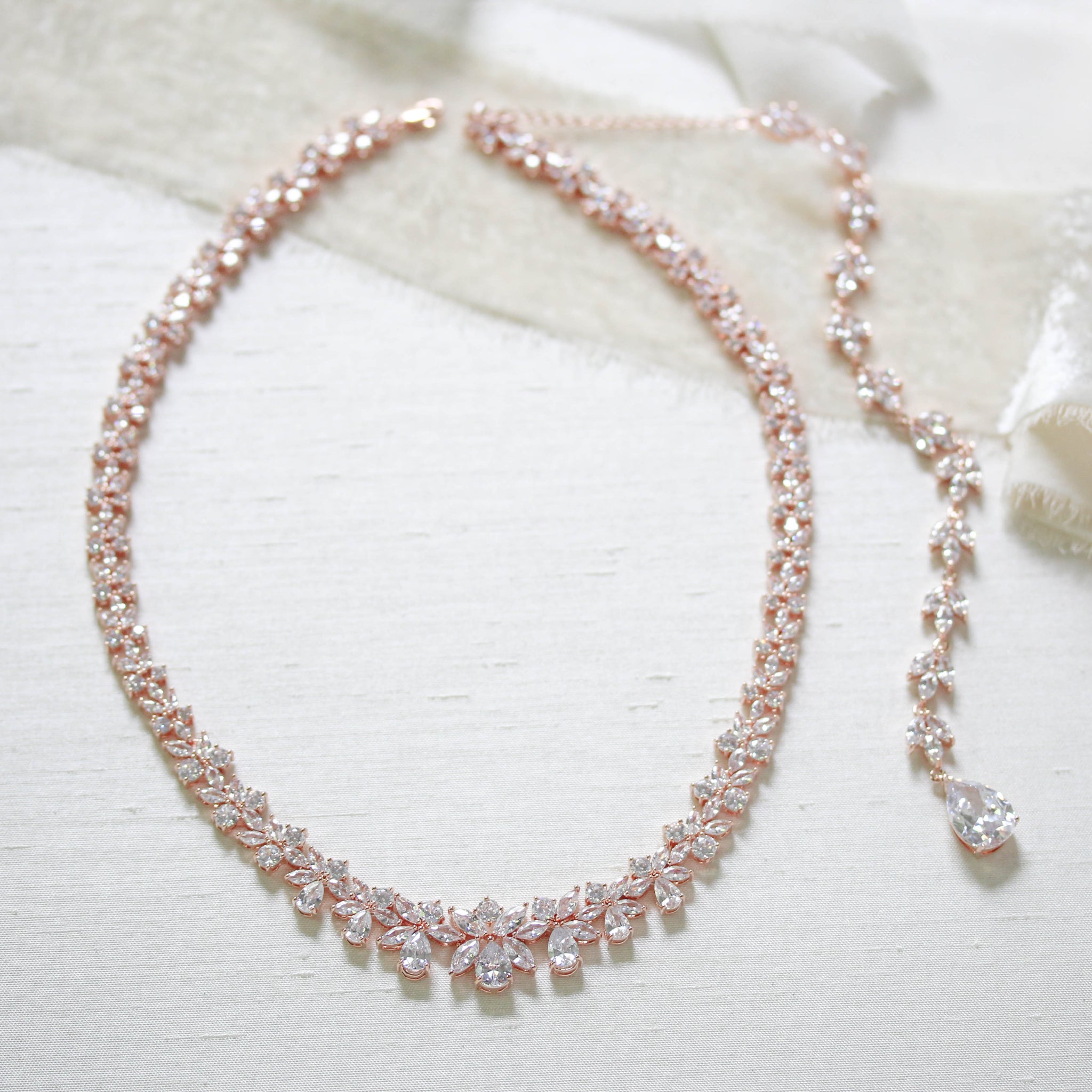 Treasures by Agnes Aubree bridal necklace with detachable cubic zirconia backdrop chain in rose gold finish displayed on ivory fabric